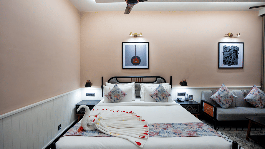 A romantic guest bedroom setup with decorative towel art arranged on the bed, soft lighting, and cosy seating beside the sleeping area | Hotel Sonar Bangla, Susunia