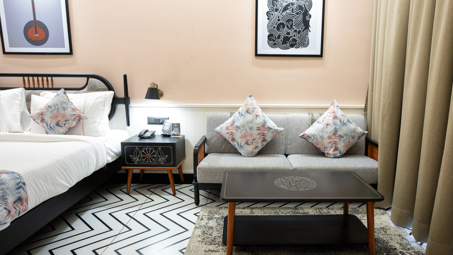 A deluxe guest room featuring a double bed, sofa seating arrangement, framed wall art, and patterned flooring with elegant interiors | Hotel Sonar Bangla, Susunia