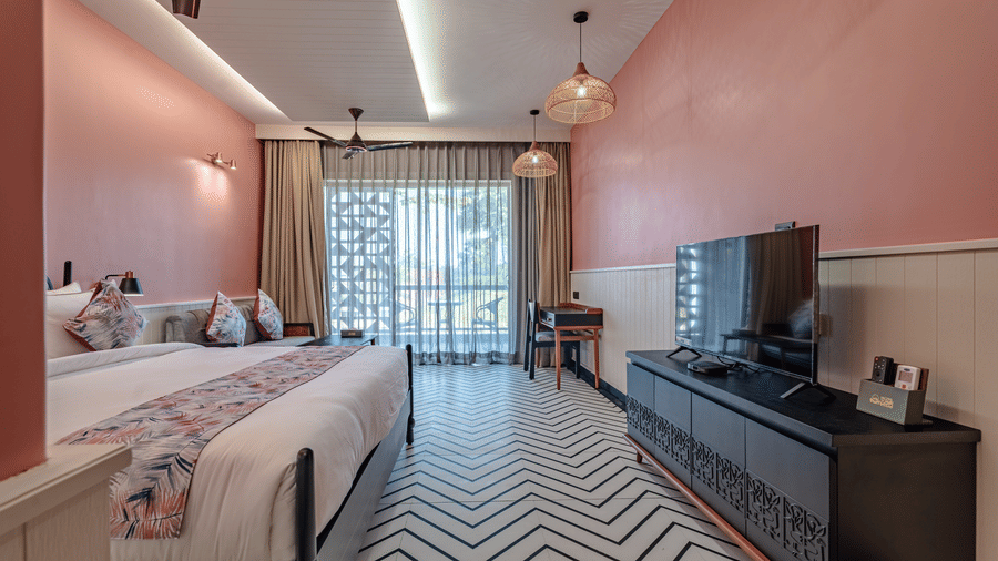 A comfortable Deluxe Room featuring a king size bed, television unit, balcony curtains, and warm ambient lighting creating a cosy atmosphere | Hotel Sonar Bangla, Susunia