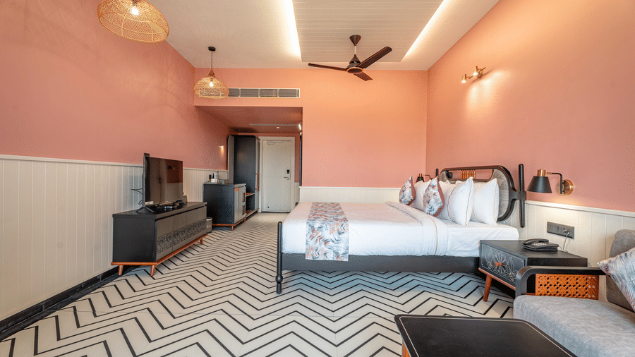 A wide-angle view of the Deluxe Room with a king size bed, seating area, television console, and elegant interiors designed with soft pastel tones | Hotel Sonar Bangla, Susunia