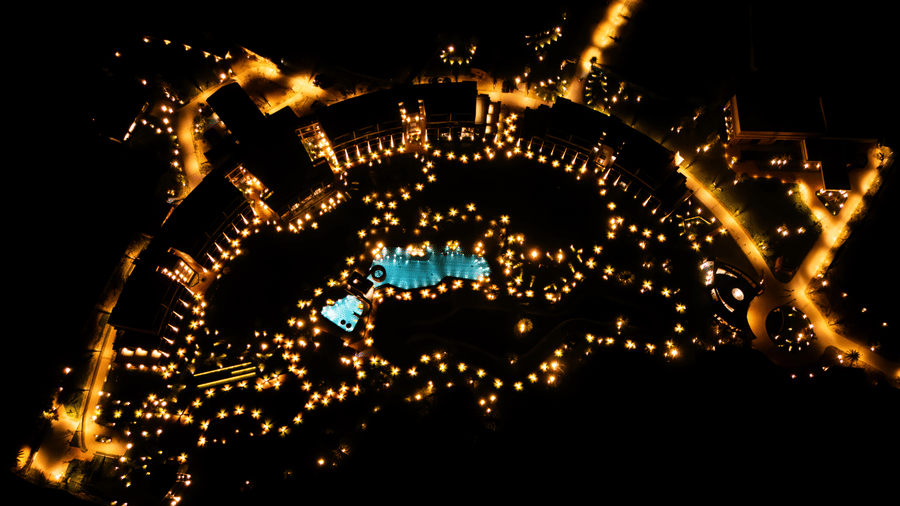 The resort complex illuminated with decorative lights at night, creating a glowing circular pattern around the swimming pool from an aerial perspective | Hotel Sonar Bangla, Susunia