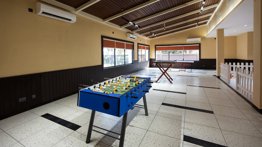An indoor recreational games room with a foosball table placed at the centre, wooden ceiling beams, and open seating areas along the sides | Hotel Sonar Bangla, Susunia