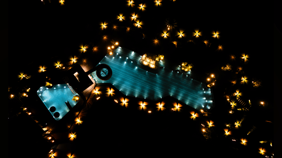 An aerial nighttime view of the glowing swimming pool surrounded by decorative warm lights spread across the resort grounds | Hotel Sonar Bangla, Susunia