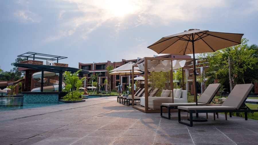Relaxing poolside sun loungers placed under large umbrellas beside the swimming pool during a warm evening at the resort | Hotel Sonar Bangla, Susunia