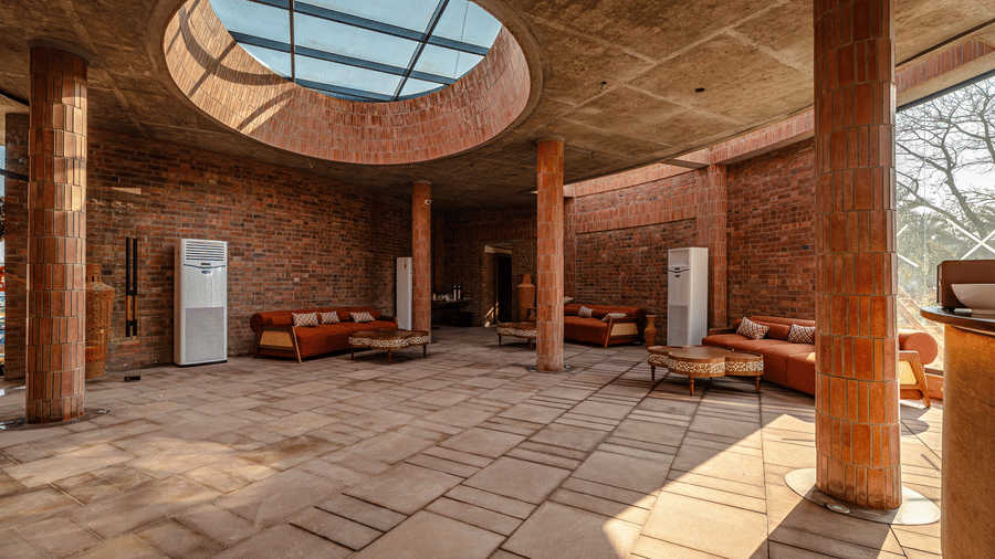 The spacious central lobby featuring stone flooring, tall pillars, lounge seating, and a large circular skylight allowing sunlight into the open interior space | Hotel Sonar Bangla, Susunia