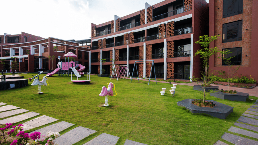 The landscaped courtyard lawn of the resort with slides for children surrounded by multi-storey guest room buildings and garden pathways | Hotel Sonar Bangla, Susunia