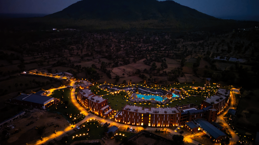 A dramatic aerial night view of the illuminated resort with glowing pathways and the dark silhouette of the Susunia Hill behind the property | Hotel Sonar Bangla