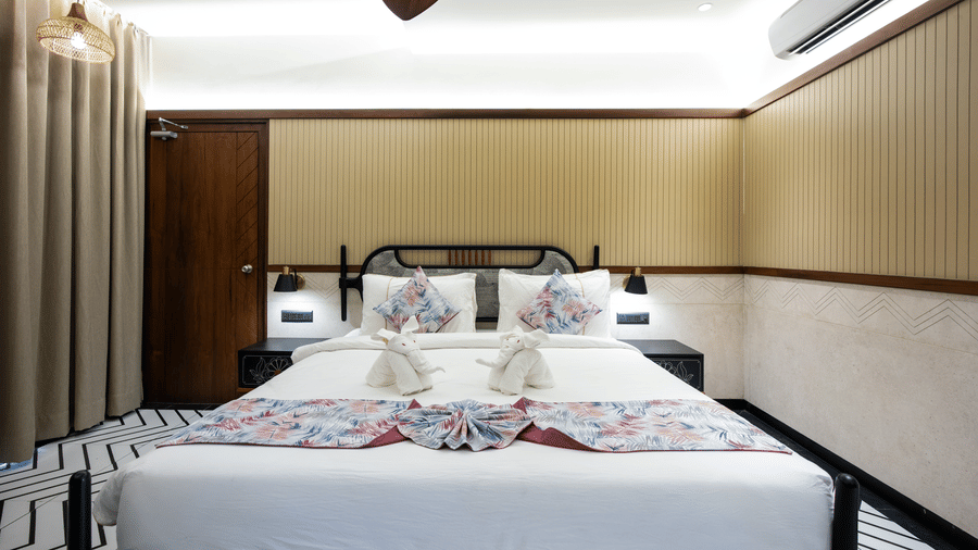 A modern deluxe bedroom featuring a large double bed with decorative cushions, soft lighting, and warm wooden interiors | Hotel Sonar Bangla, Susunia