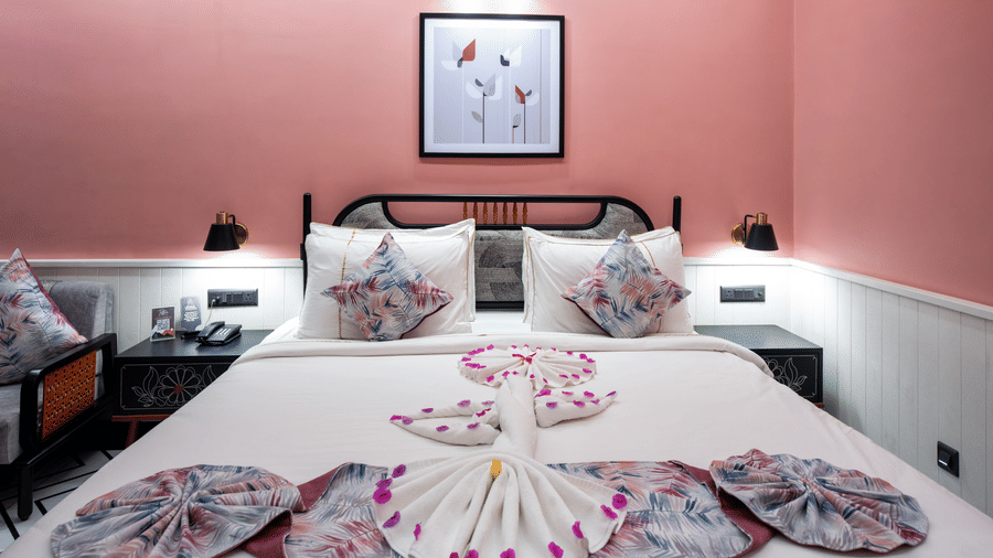 A cosy guest bedroom in our Susunia Suite decorated with flower petals and towel art arranged beautifully on the bed against a soft pink accent wall | Hotel Sonar Bangla
