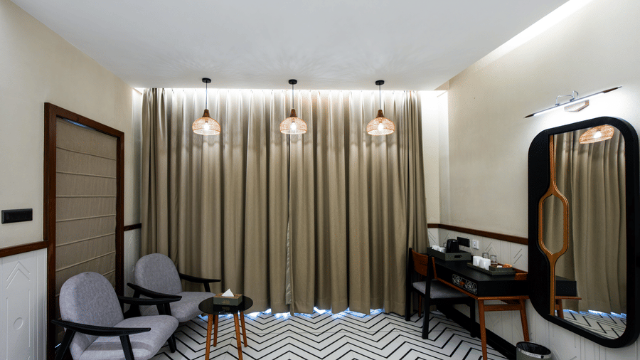A spacious guest room in Susunia with elegant seating chairs, a centre table, long curtains, and a dressing mirror placed beside the work desk area | Hotel Sonar Bangla