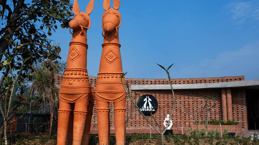 Large traditional tribal-inspired sculptures placed beside the brick entrance facade of the resort against a blue sky backdrop | Hotel Sonar Bangla, Susunia