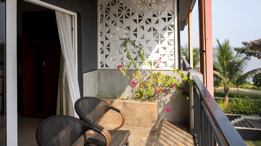 Balcony setup with chairs, flowers, black railing, and a pattern wall design at Hotel Sonar Bangla, Taki.