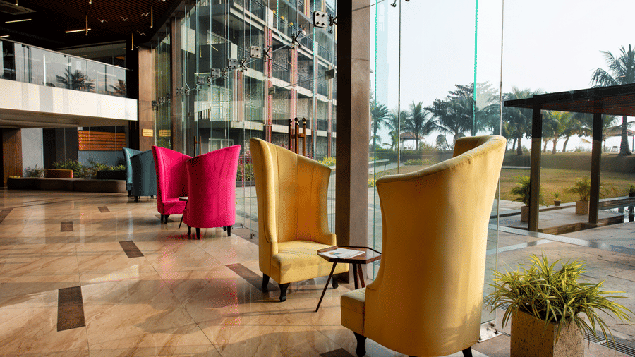Alternate pairs of chairs placed on either sides of a mini table beside floor to ceiling windows at Hotel Sonar Bangla, Taki.
