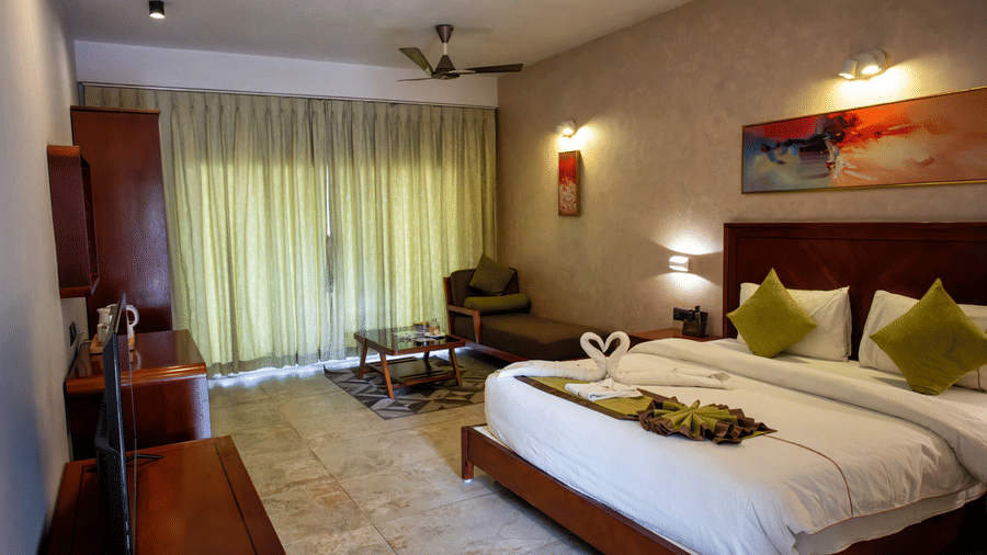 Room featuring green curtains, a large bed, 2 fans, a painting above the bed, and swan shaped towels kept at the foot of the bed at Hotel Sonar Bangla, Taki.