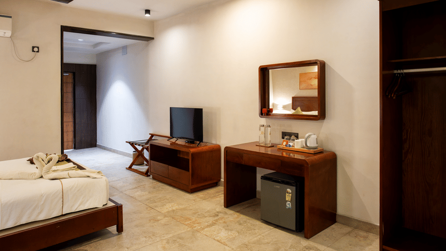 Well-furnished room with a bed, television kept on a wooden stand, a mirror, a table, and a minibar placed under it at Hotel Sonar Bangla, Taki. 