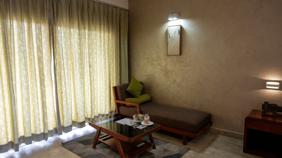 Deluxe room with green curtains, a wooden table, and a small bed against a wall at Hotel Sonar Bangla, Taki.