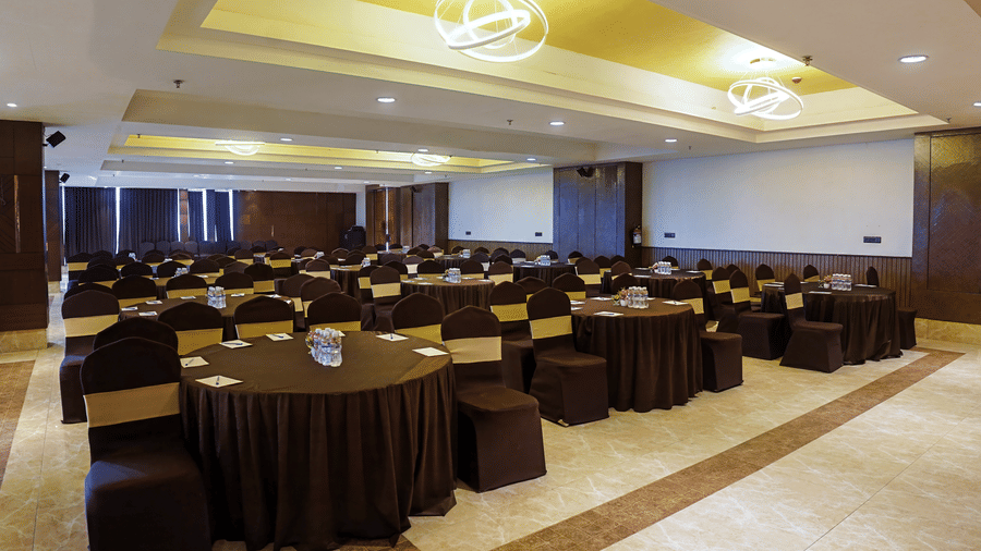 Grand hall with round tables and dark chair covers ready for a dinner at Hotel Sonar Bangla, Taki.