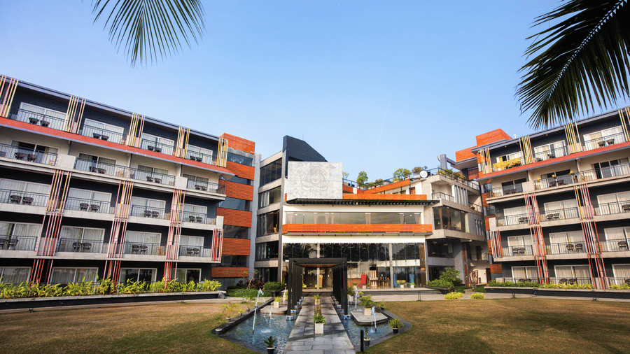 Front exterior of Hotel Sonar Bangla, Taki, featuring vibrant architecture, a fountain, and lush garden pathways under a clear sky.