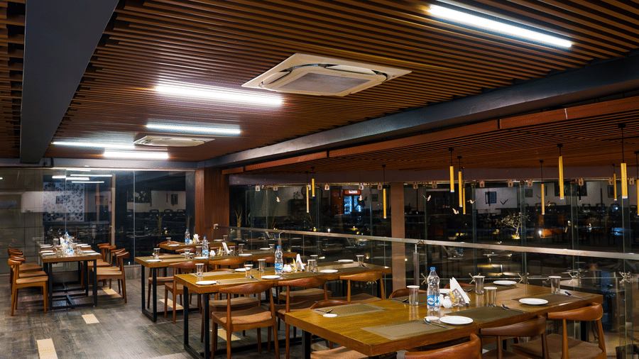 Restaurant interior with wooden ceiling, dining tables, and ambient lighting at Hotel Sonar Bangla, Taki.