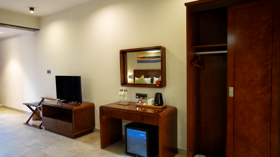 A well-furnished room with a television on a wooden table and a minibar beside a wardrobe at Hotel Sonar Bangla, Taki.