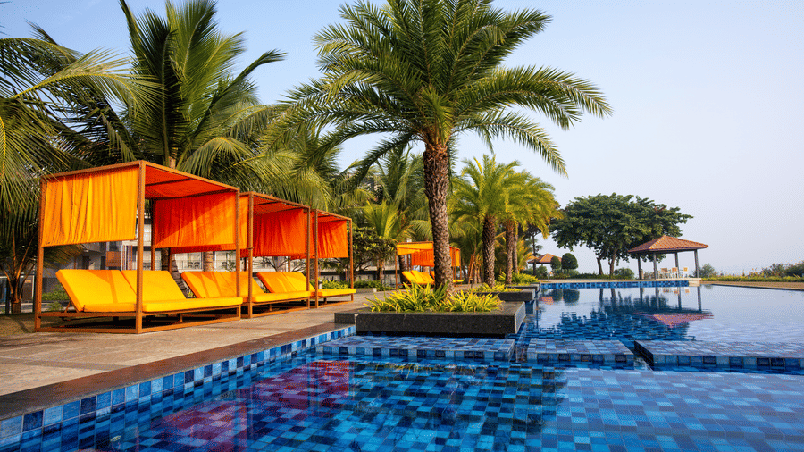 Outdoor swimming pool featuring orange sun loungers and palm trees at Hotel Sonar Bangla, Taki.