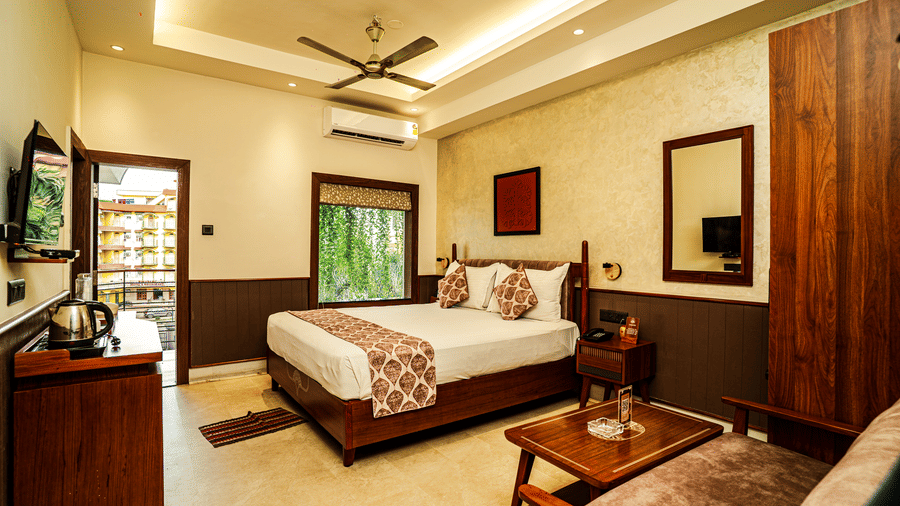 A hotel bedroom with a large double bed, seating area, wooden wardrobe, and balcony overlooking greenery | Hotel Sonar Bangla, Tarapith