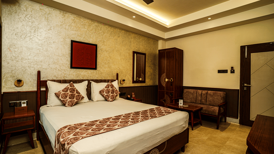 The Deluxe Room featuring a double bed, a sofa, a wooden wardrobe, beside stands, and warm lighting | Hotel Sonar Bangla, Tarapith