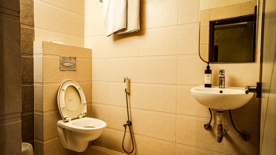 A modern hotel bathroom with toilet, wash basin, mirror, towel rack, and beige tiled walls | Hotel Sonar Bangla, Tarapith