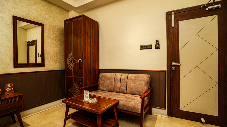 The seating area of the Deluxe Double Bedded Room featuring a couch, a coffee table, a wooden wardrobe, and a mirror | Hotel Sonar Bangla, Tarapith
