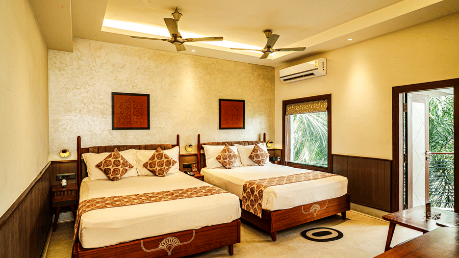 The Deluxe Room featuring twin beds, wooden decor, a seating area, and an attached balcony | Hotel Sonar Bangla, Tarapith