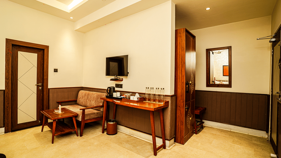 The seating area in the living room featuring a wall-mounted television, a cosy sofa with a coffee table, and a wooden wardrobe | Hotel Sonar Bangla, Tarapith