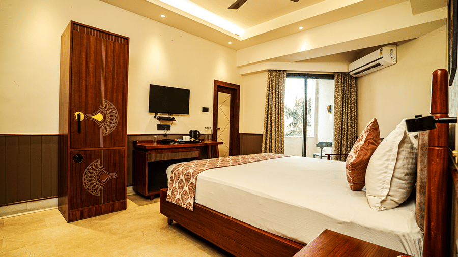 The bedroom of our Deluxe Suite in Tarapith featuring a double bed, a wall-mounted television, a wardrobe, and a balcony | Hotel Sonar Bangla, Tarapith