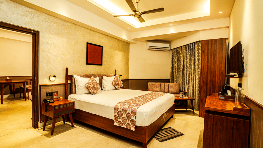 The bedroom of our Deluxe Suite featuring a double bed, a wall-mounted television, a sofa, and the doorway leading to the living room | Hotel Sonar Bangla, Tarapith