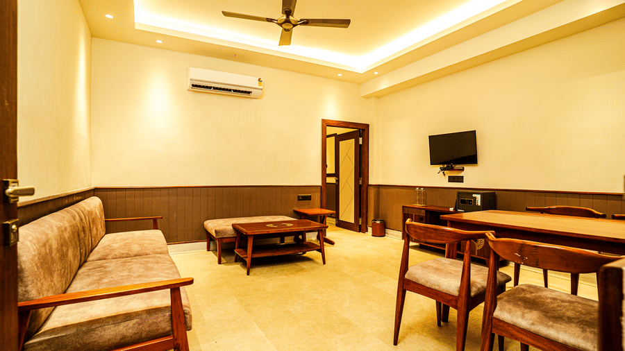 The living area in our hotel room in Tarapith featuring a cosy cushioned couch, a dining area, a coffee table, and a wall-mounted television | Hotel Sonar Bangla