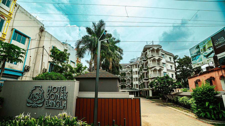 Entrance view of Hotel Sonar Bangla, Tarapith, with landscaped greenery, palm trees, and the hotel sign near the driveway.