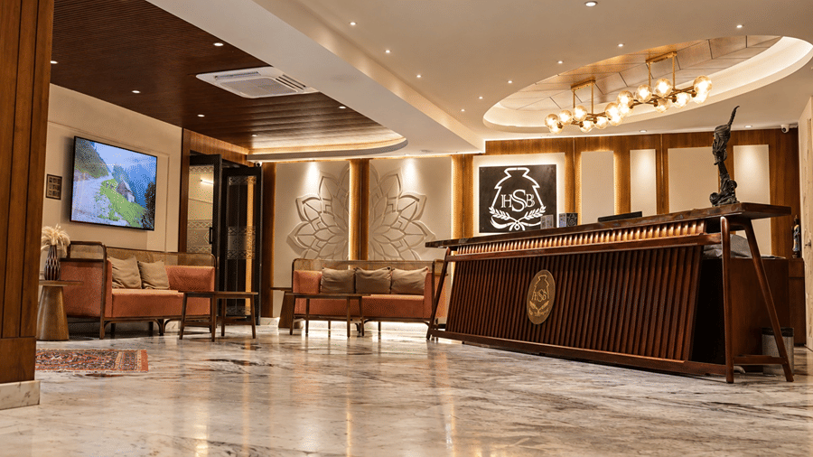 A reception lobby at Hotel Sonar Bangla, Tarapith featuring a wooden counter, seating area, chandelier, wall art, and polished floor.