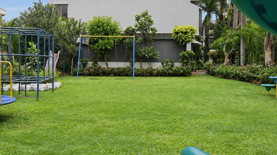 A spacious lawn at Hotel Sonar Bangla, Tarapith featuring climbing frames, swing set, greenery, hedges, and hotel building backdrop.