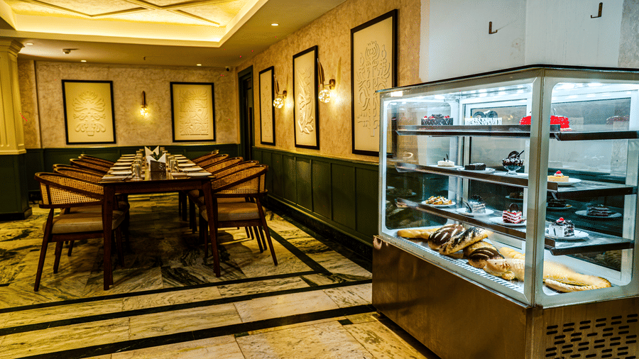 A seating area in our Tarapith restaurant featuring a pastry display counter, dining tables, and softly illuminated interiors | Hotel Sonar Bangla, Tarapith