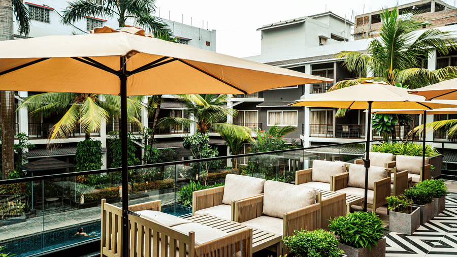 A close up of the couches at Sundowner Cafe featuring overhead sunshades overlooking the pool | Hotel Sonar Bangla, Tarapith