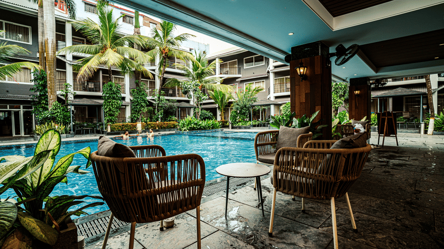 Comfortable lounge chairs and a coffee table arranged in the outdoor seating area of Sundowner Cafe overlooking the swimming pool | Hotel Sonar Bangla, Tarapith