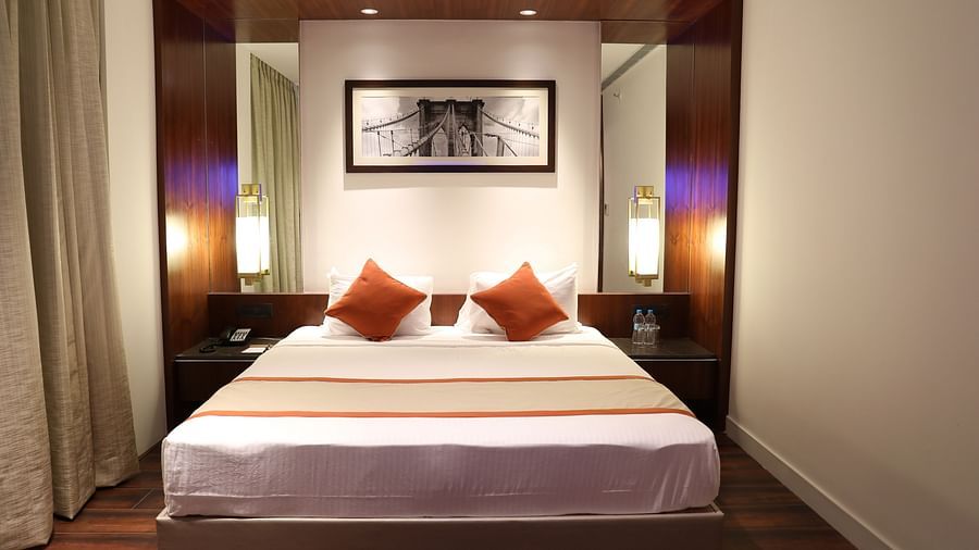 The front view of a hotel room with a large bed, white linens, burnt orange accents and a framed picture of a bridge above the headboard - Hotel Southend by TGI - Bommasandra, Bangalore