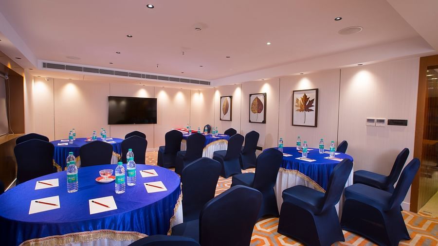 An intimate boardroom setting with round tables covered in blue cloth, blue chairs and a large flat-screen TV - Hotel Southend by TGI - Bommasandra, Bangalore