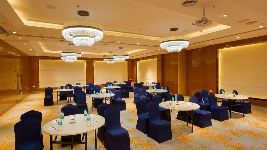 A conference room arranged with round tables, blue chairs and bottles of water, under elegant chandeliers - Hotel Southend by TGI - Bommasandra, Bangalore