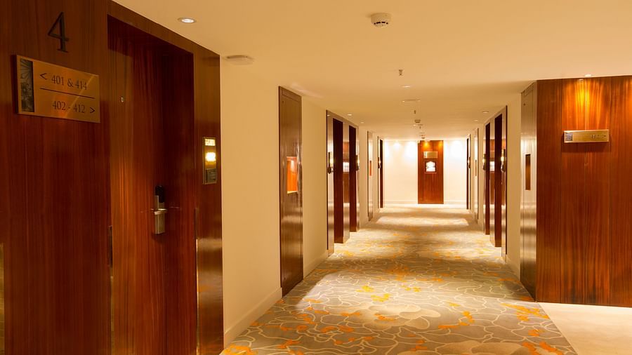 A warmly lit hotel corridor with wooden doors and carpeted floor displaying room numbers - Hotel Southend by TGI - Bommasandra, Bangalore