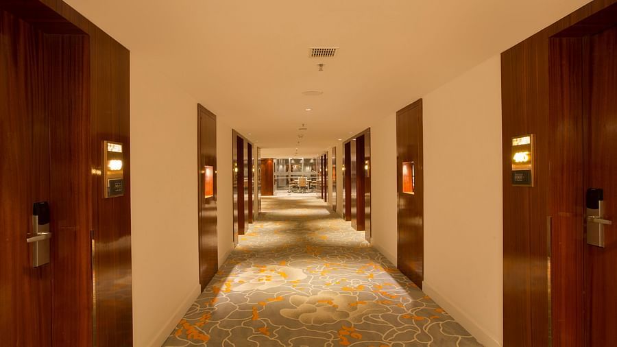 A long hotel corridor with wooden doors and a patterned carpet leading towards a well-lit area - Hotel Southend by TGI - Bommasandra, Bangalore