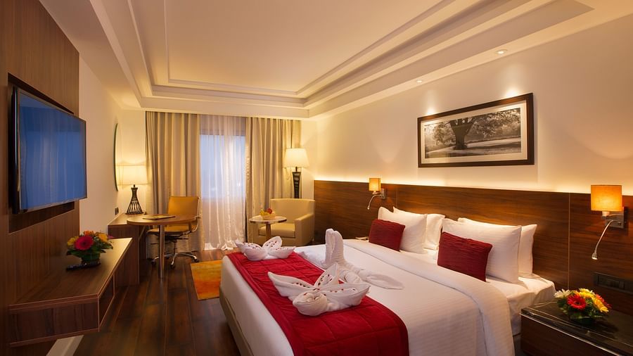 An elegant hotel room with a large bed, red throw blanket, decorative pillows and a framed black-and-white photograph on the wall - Hotel Southend by TGI - Bommasandra, Bangalore