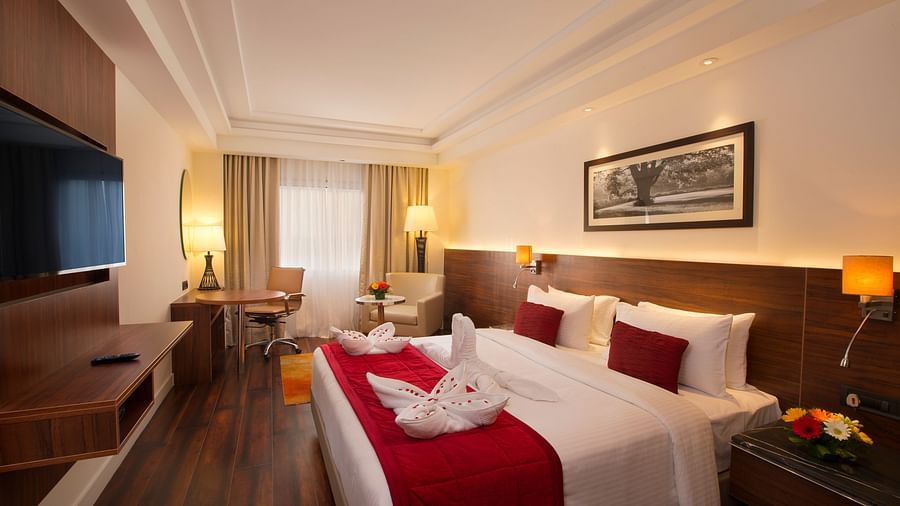 An elegant hotel room with a large bed, red throw blanket, decorative pillows and a framed black-and-white photograph on the wall - Hotel Southend by TGI - Bommasandra, Bangalore