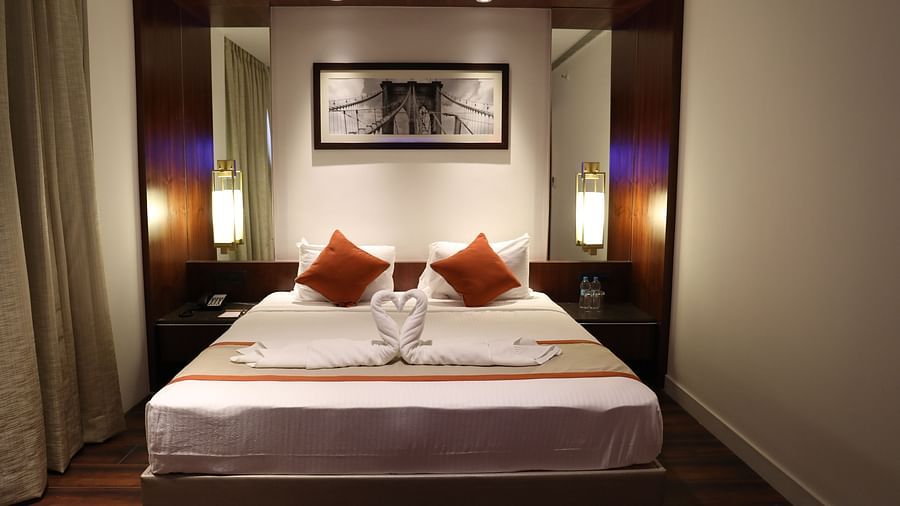 The front view of a hotel room with a large bed, white linens, burnt orange accents and a framed picture of a bridge above the headboard - Hotel Southend by TGI - Bommasandra, Bangalore