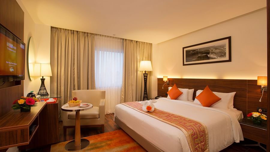A hotel room featuring a large bed with white and orange linens, a work desk and a black-and-white photo of a landscape on the wall - Hotel Southend by TGI - Bommasandra, Bangalore