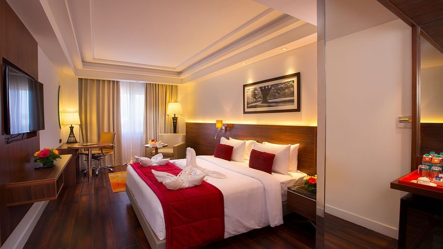 Another view of an elegant hotel room with a large bed, red throw blanket, decorative pillows and a framed black-and-white photograph on the wall - Hotel Southend by TGI - Bommasandra, Bangalore